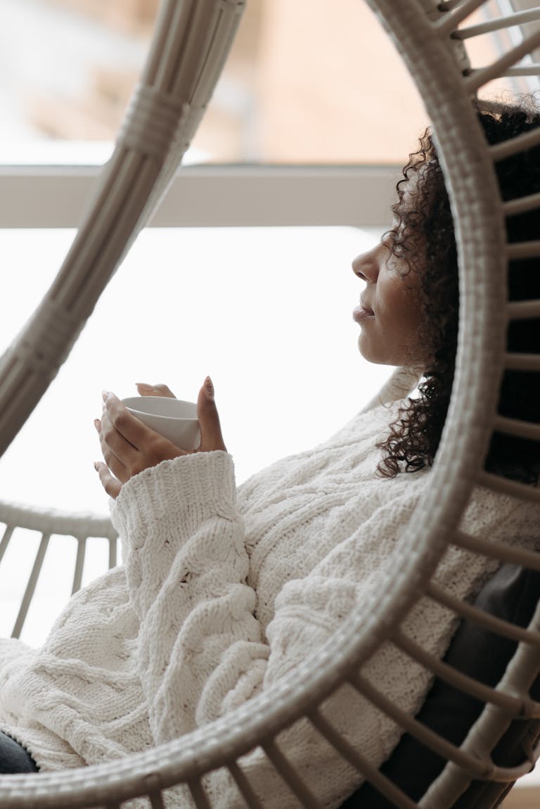 Peaceful woman with curly hair enjoys coffee in a stylish indoor setting, captured in profile view.