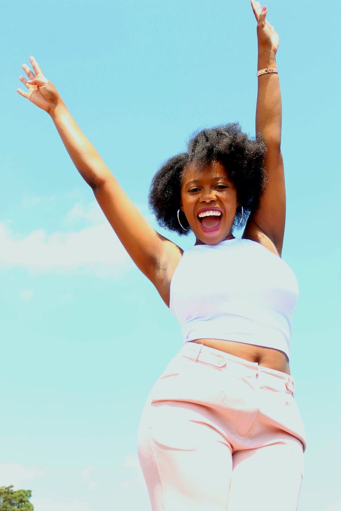 Young woman joyfully celebrating outdoors under a clear blue sky, expressing happiness and freedom.