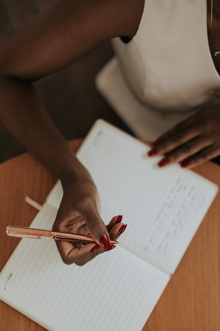 A close-up of a woman writing in a lined notebook, focusing on her hand and pen.